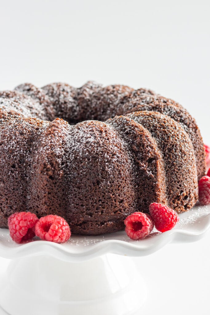 A whole Chocolate Brownie Bundt Cake with fresh raspberries around the edge of the cake.