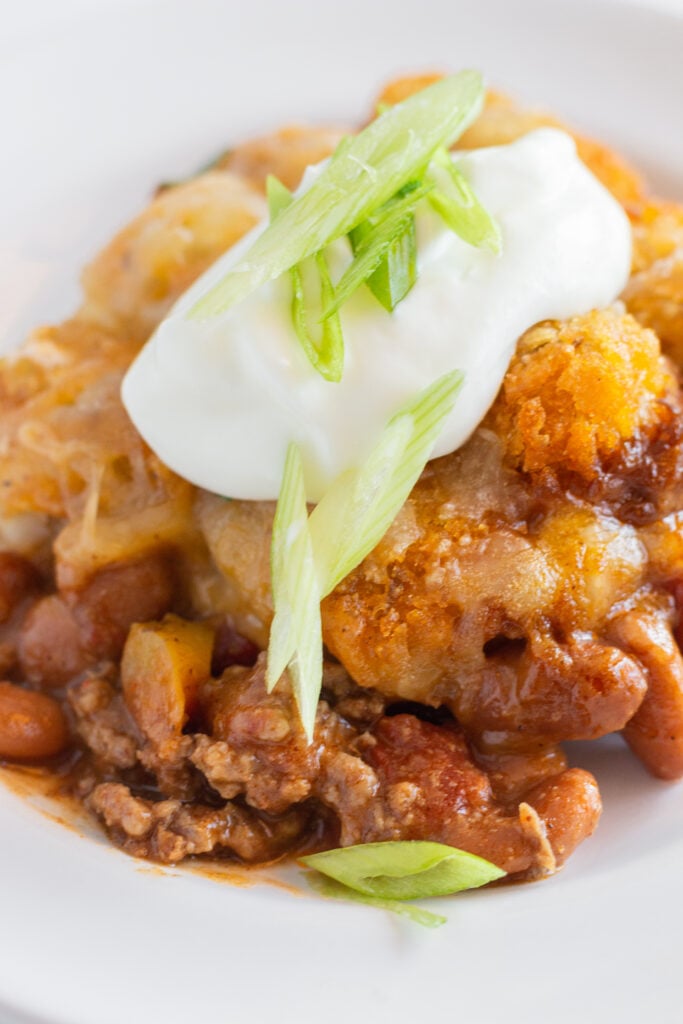 A single serving of Chili Tater Tot Casserole with sour cream and green onion toppings.