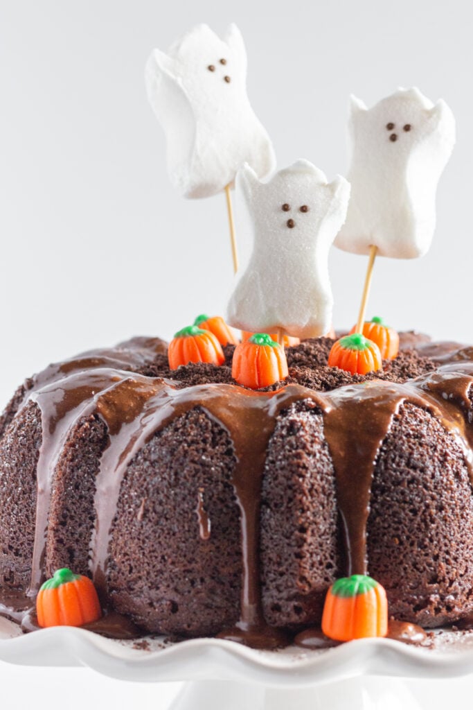 Close up photo of a Halloween Bundt Cake decorated with ghost peeps and candy pumpkins.