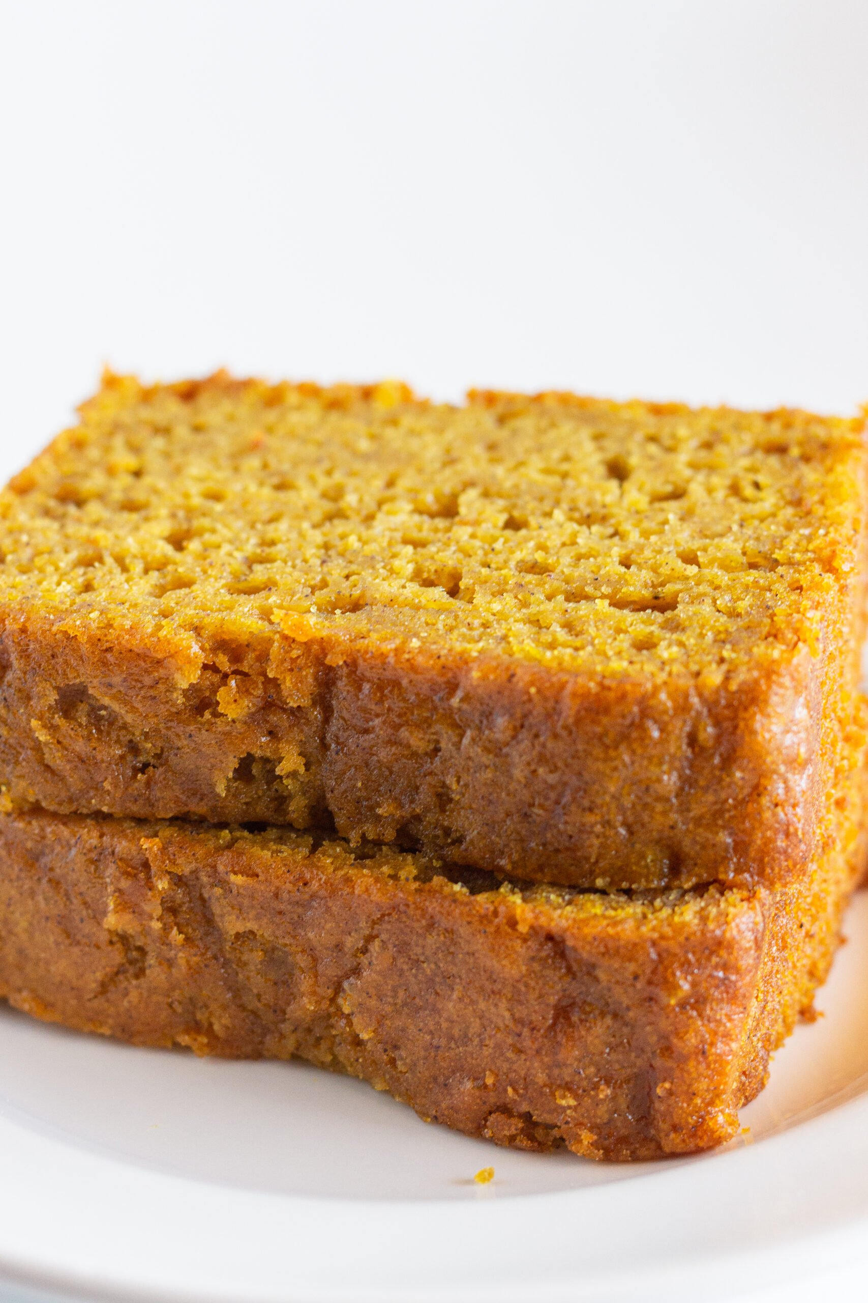 Two slices of pumpkin bread stacked on top of each other on a white plate.