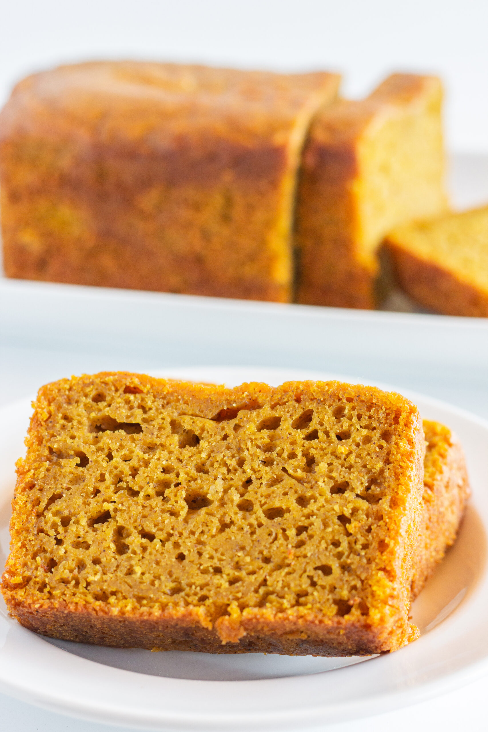 Two slices of pumpkin bread on a white plate with a loaf of pumpkin bread in the background.