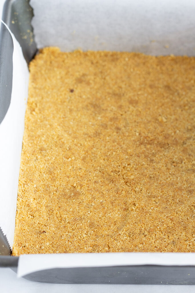 A graham cracker crust in a parchment lined baking pan.