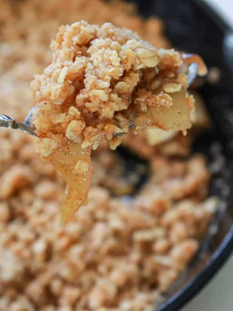 A spoon lifting a bite of apple crisp out of a cast iron skillet.