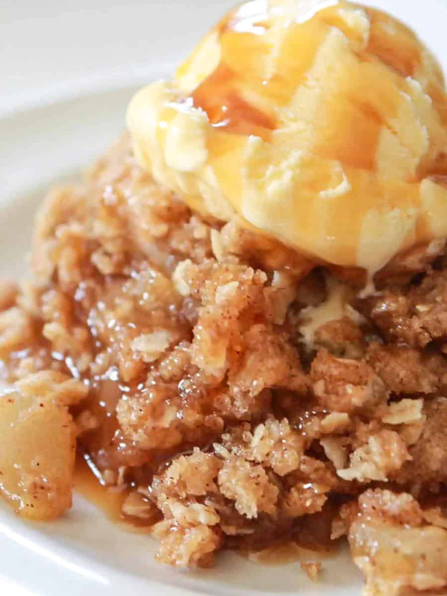 A serving of Skillet Apple Crisp with a scoop of vanilla ice cream and a drizzle of caramel sauce.
