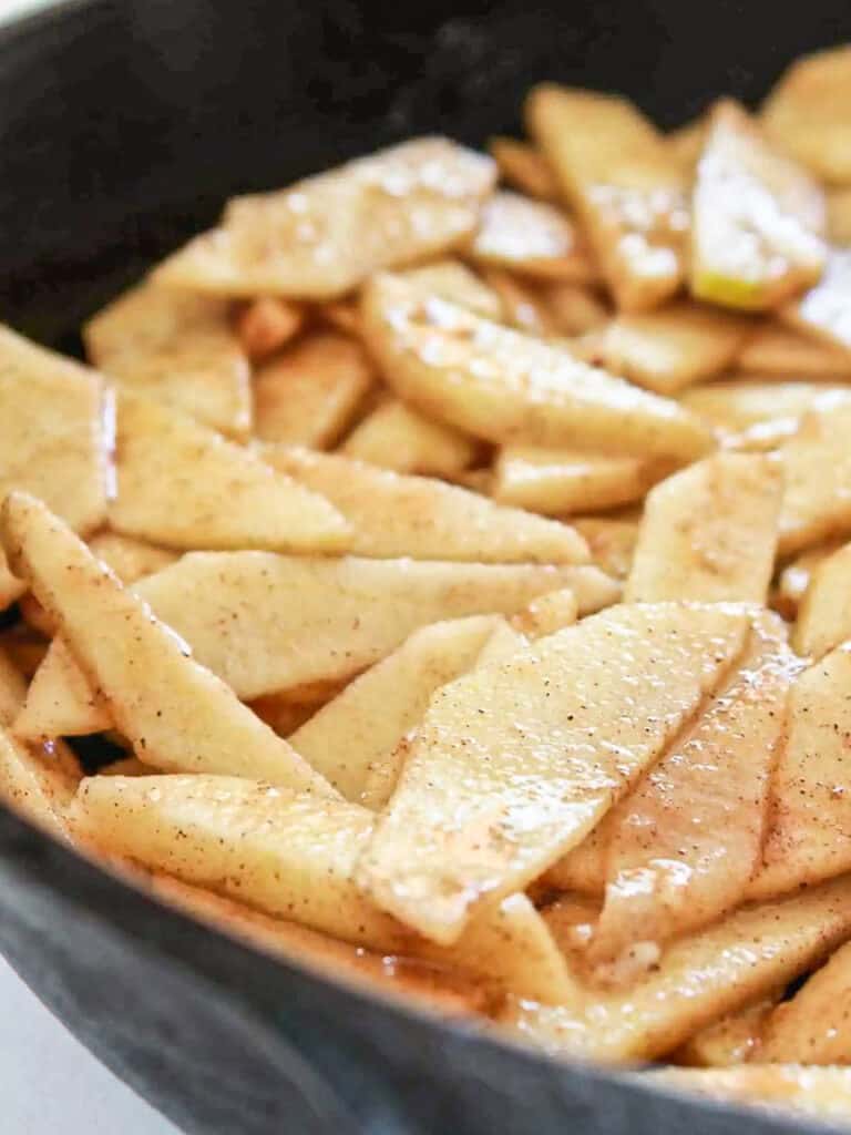 Thinly sliced apples cooked with spices in a cast iron skillet.