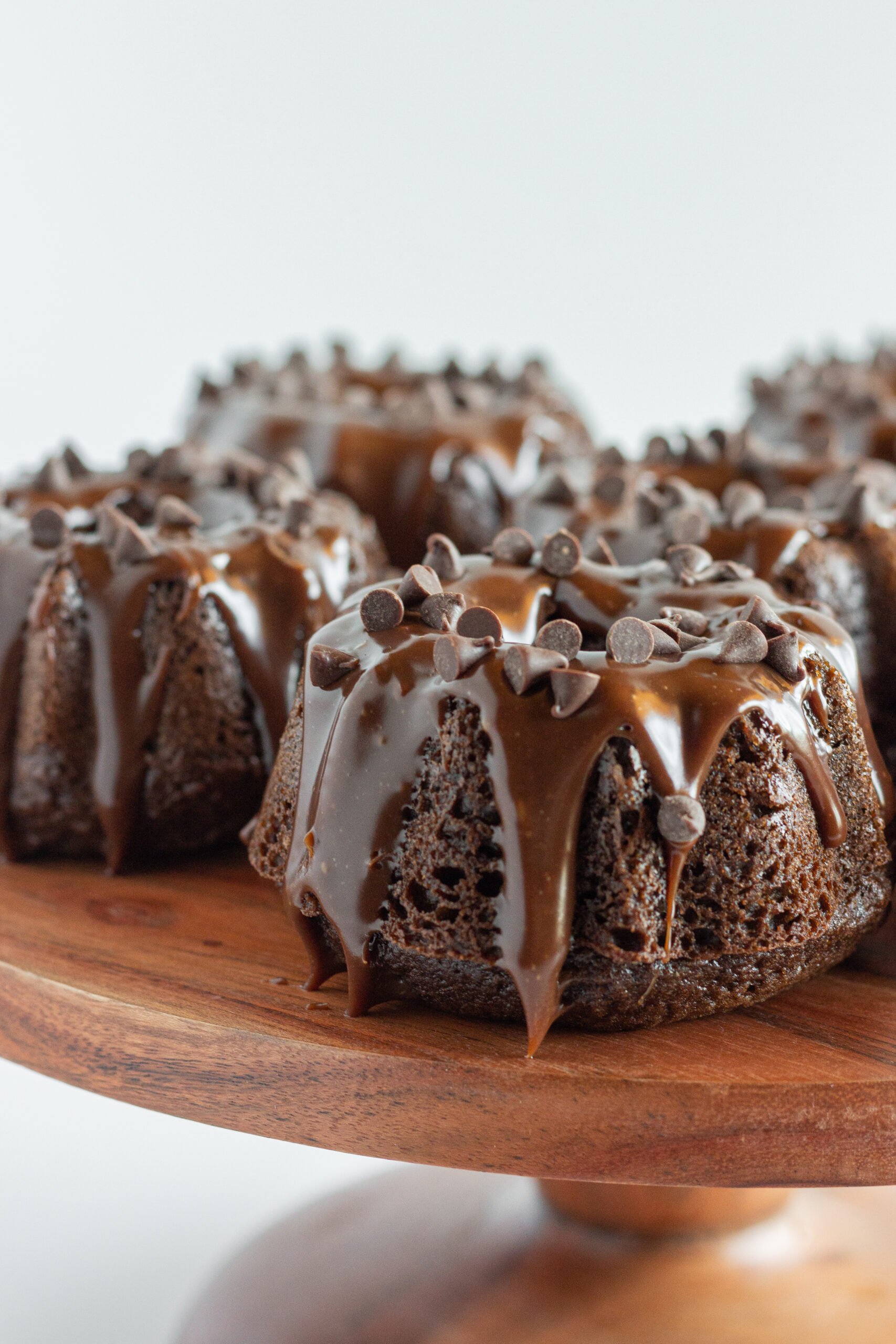 Several Mini Chocolate Bundt Cakes on a wood cake plate.