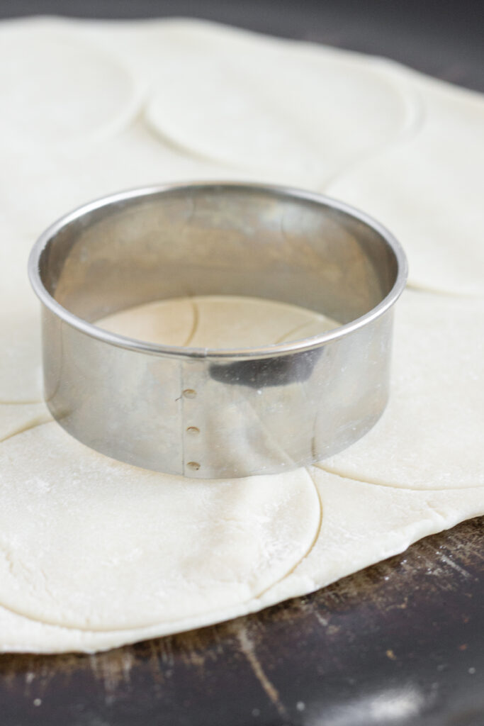 A round cookie cutter on top of pie crust dough.