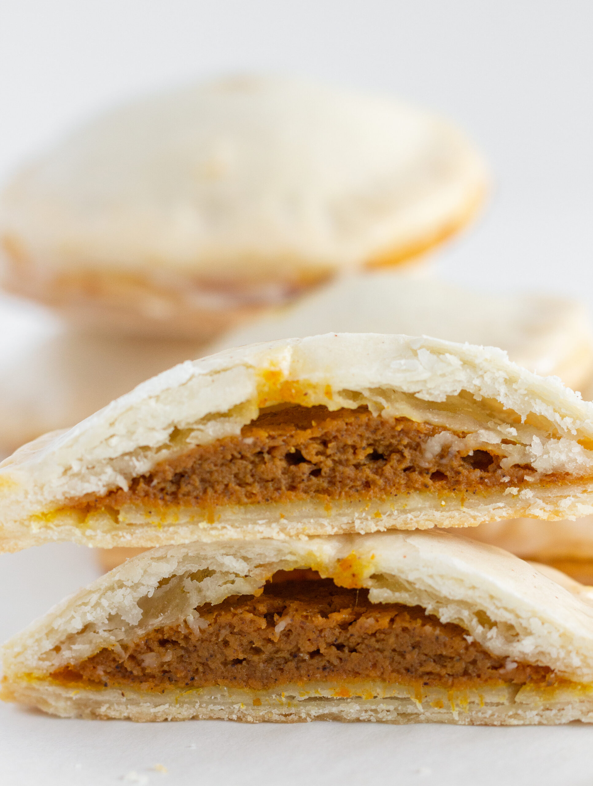 Stacks of Pumpkin Hand Pies with one cut open to see the pumpkin pie filling in the middle.