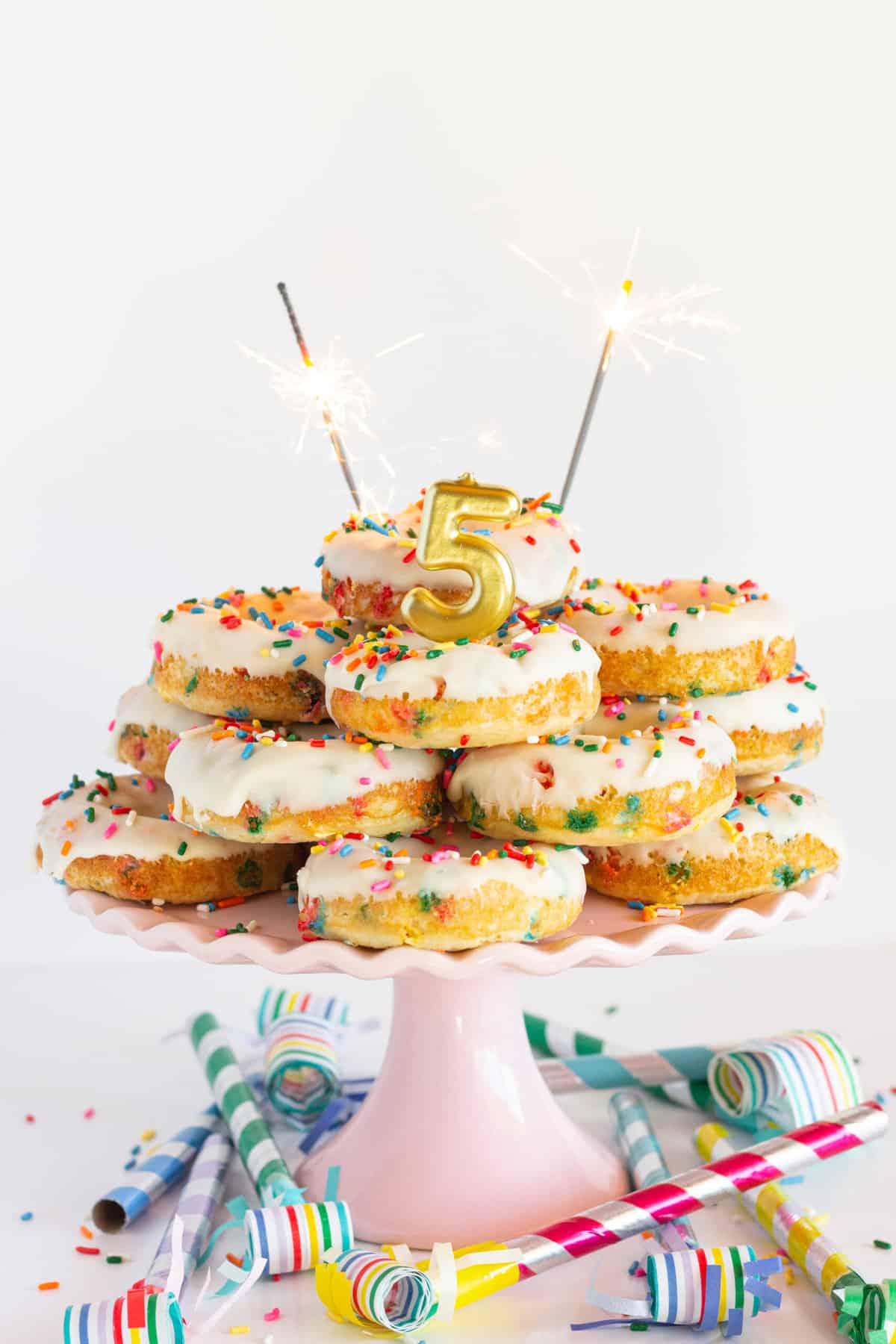 A cake plate with donuts stacked like a cake and 5 candle with sparklers lit.