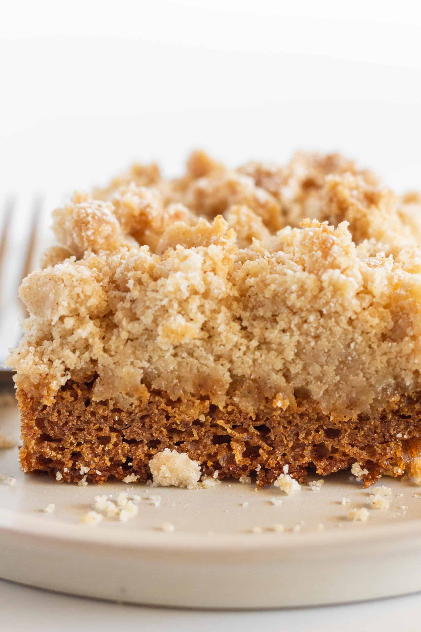 A square of gingerbread coffee cake on a white plate with a fork.