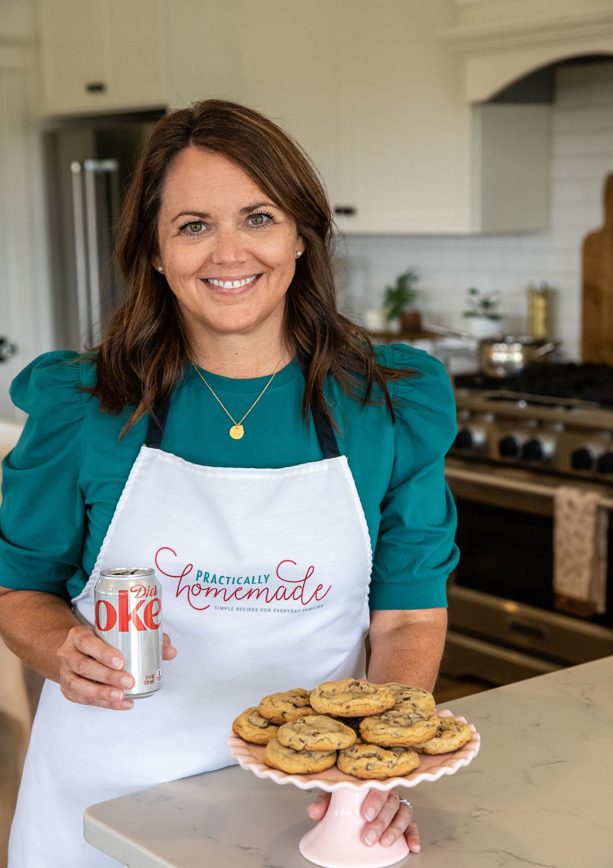A photo of June in the kitchen with a Diet Coke in her hand and a plate of chocolate chip cookies.