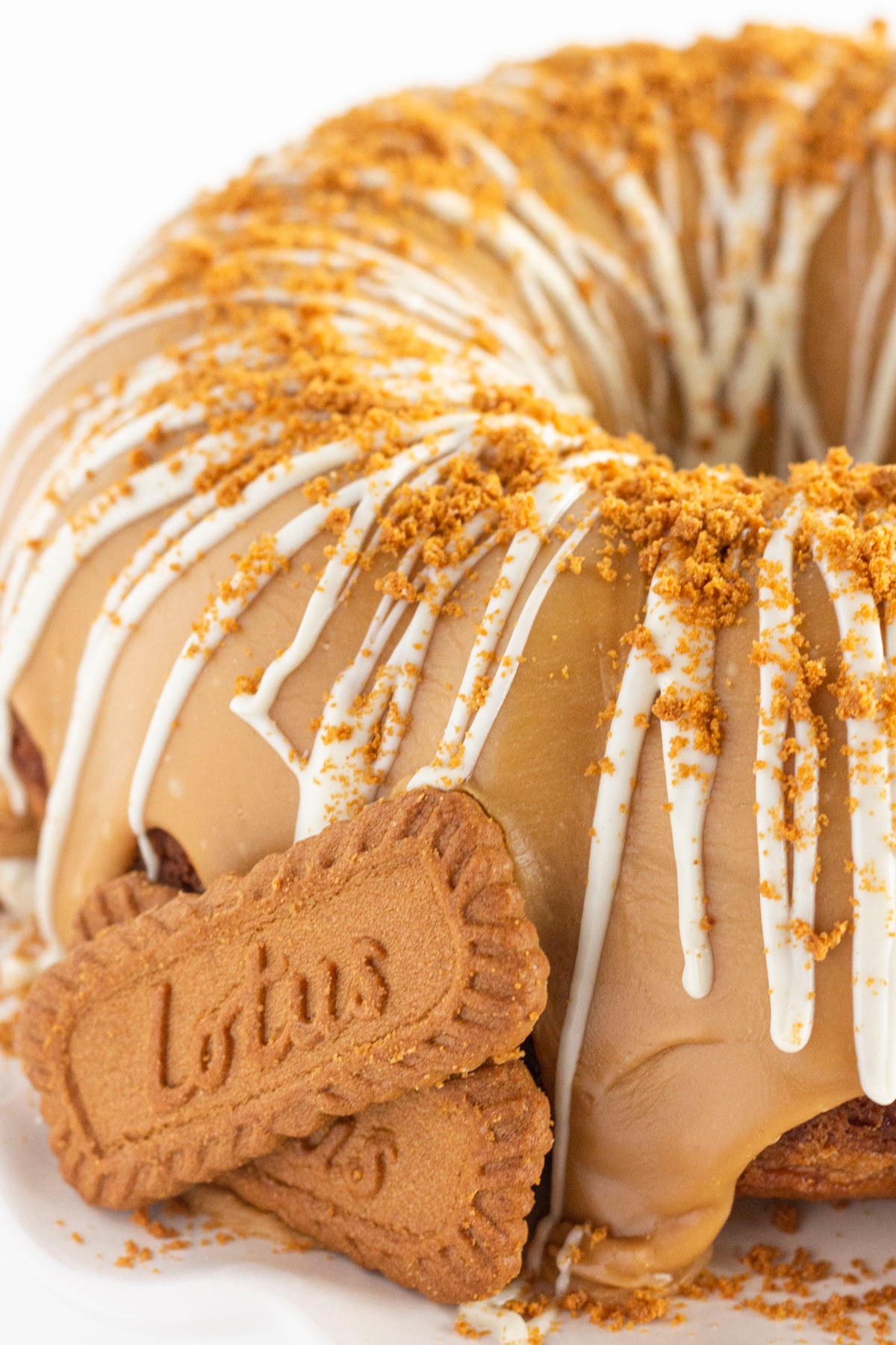 A whole cookie butter bundt cake with frosting, a drizzle of white chocolate and cookie crumbs.
