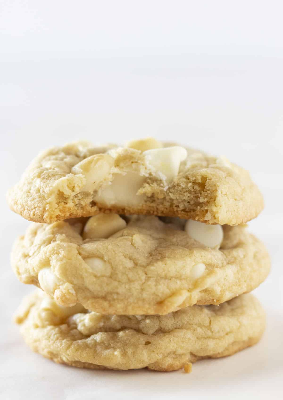 Three White Chocolate Macadamia Nut Cookies stacked on top of each other with a bite taken out of the top one.
