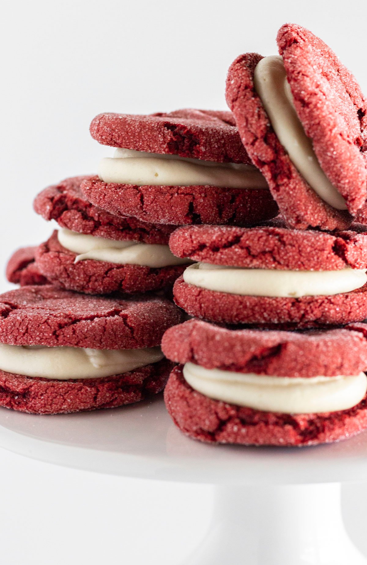 A white cake plate with red velvet sandwich cookies stacked on top.