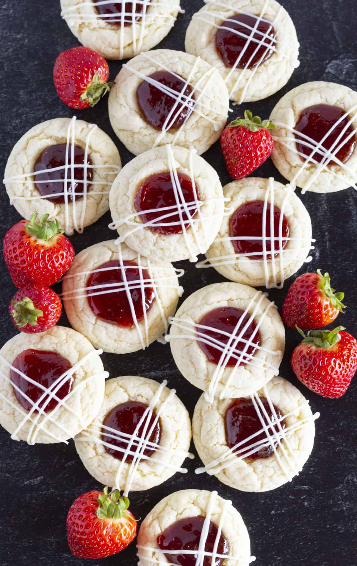 A dozen Strawberry Jam Cookies on a black tray with fresh strawberries.