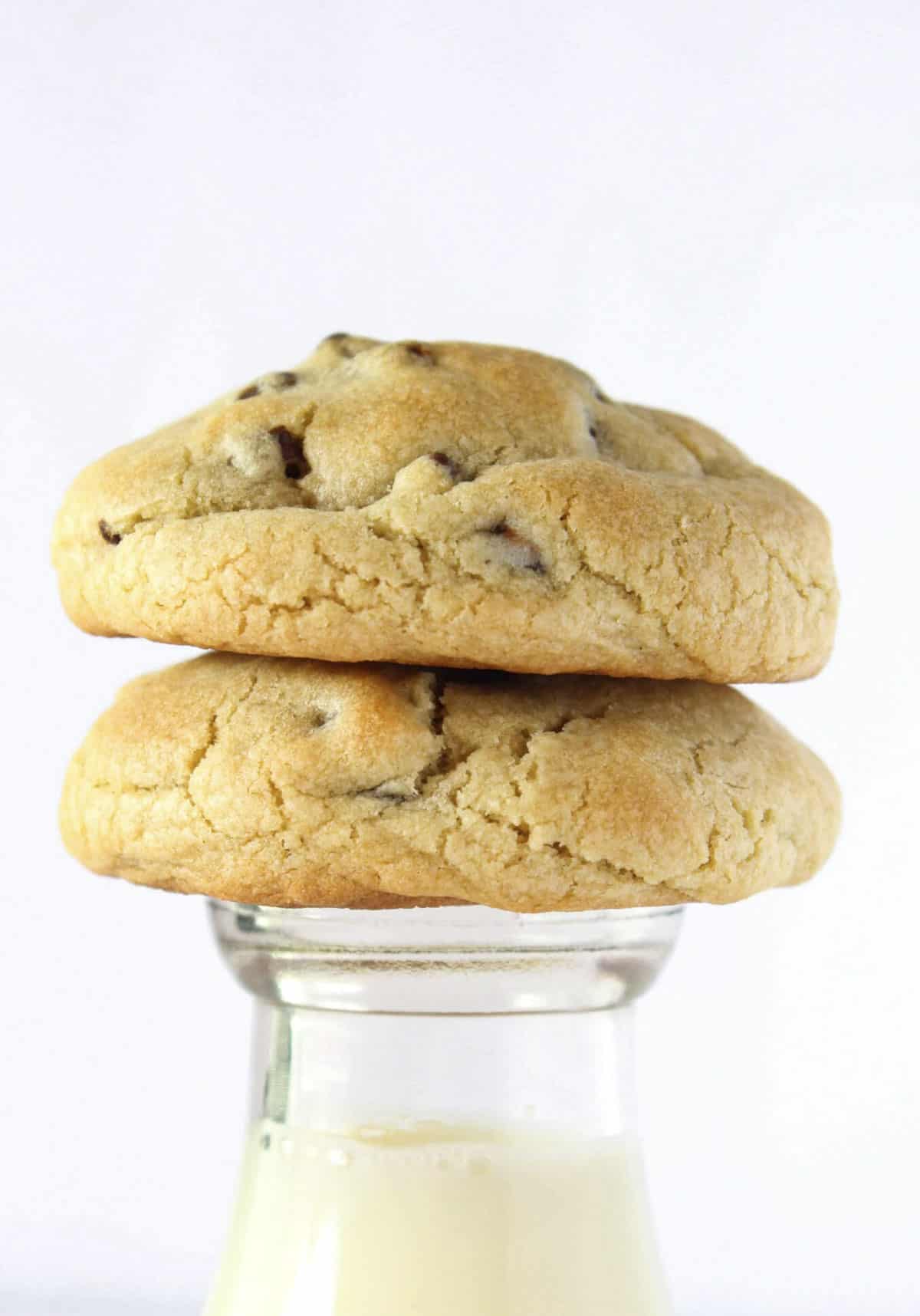 Two Thick Chocolate Chip Cookies on top of an antique milk bottle filled with milk.