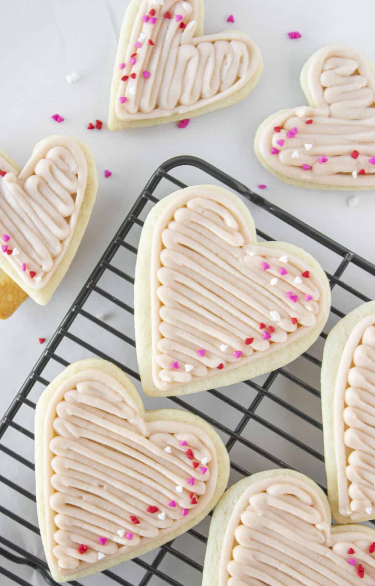Looking down on heart shaped cookies with strawberry buttercream on a cooling rack.