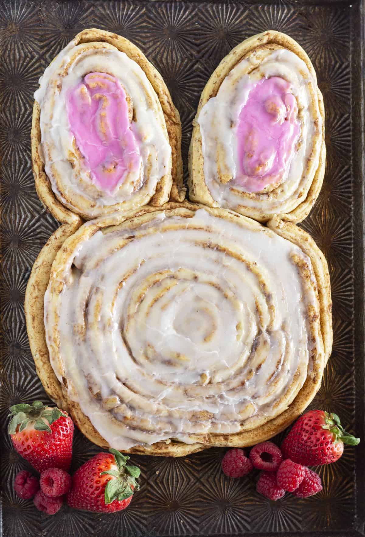 A giant bunny cinnamon roll made with refrigerated cinnamon rolls and served with strawberries and raspberries.