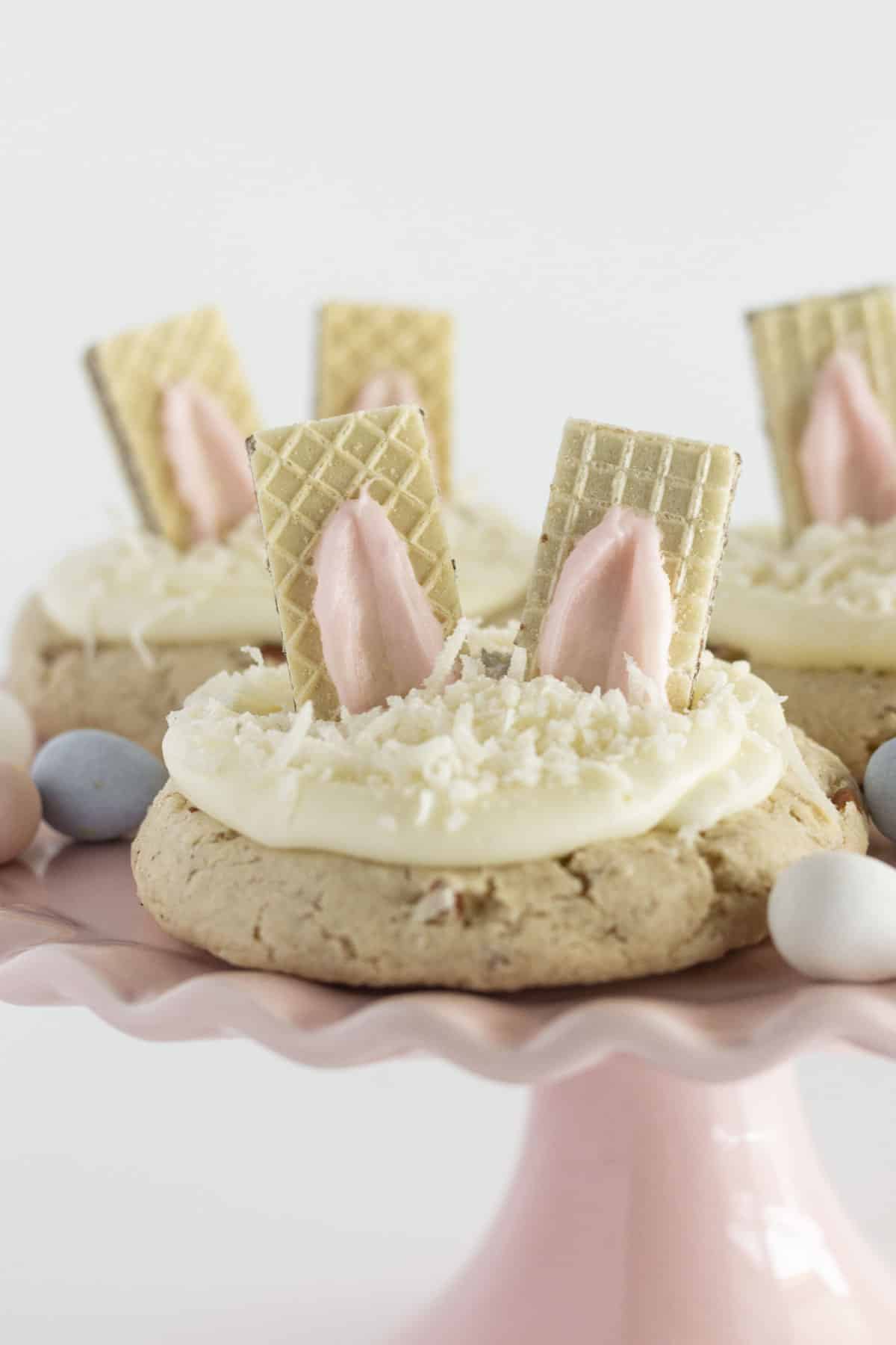 A large pink cake plate with three bunny cookies and chocolate eggs.
