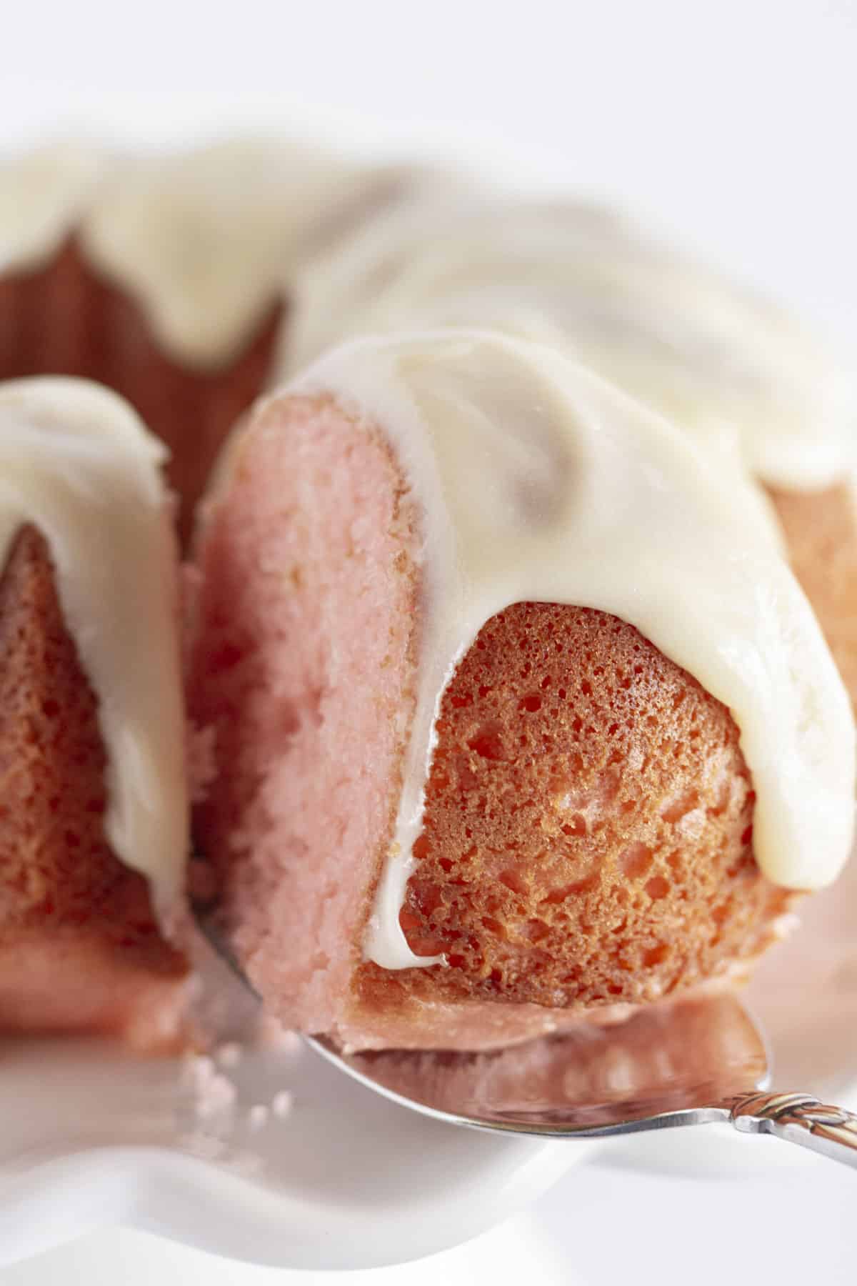 Taking a slice of cake from a whole pink velvet bundt cake.