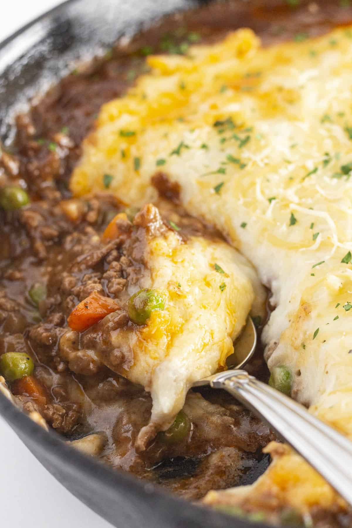 A close up photo of the cast iron shepherd's pie with a spoon in it for serving.