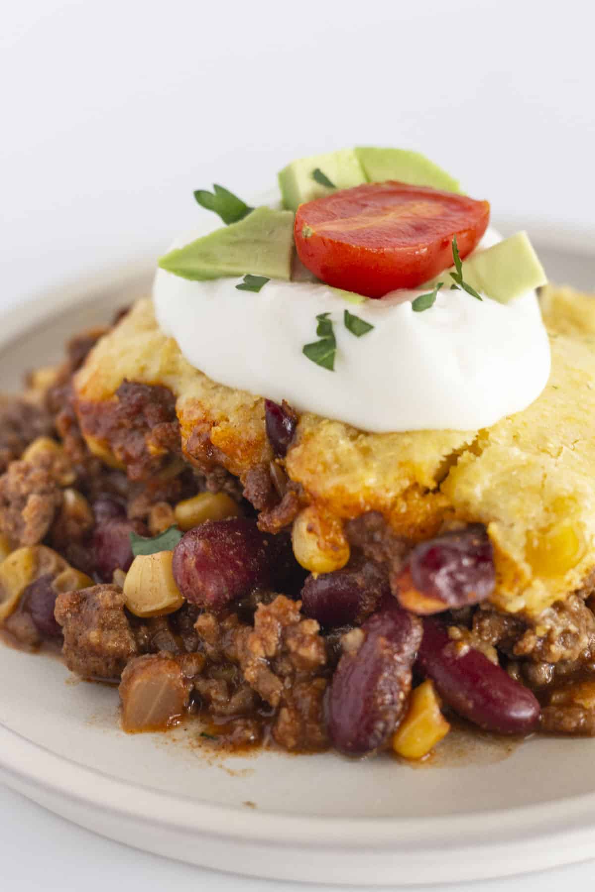 A serving of cowboy cornbread casserole, topped with sour cream, tomato and avocado.