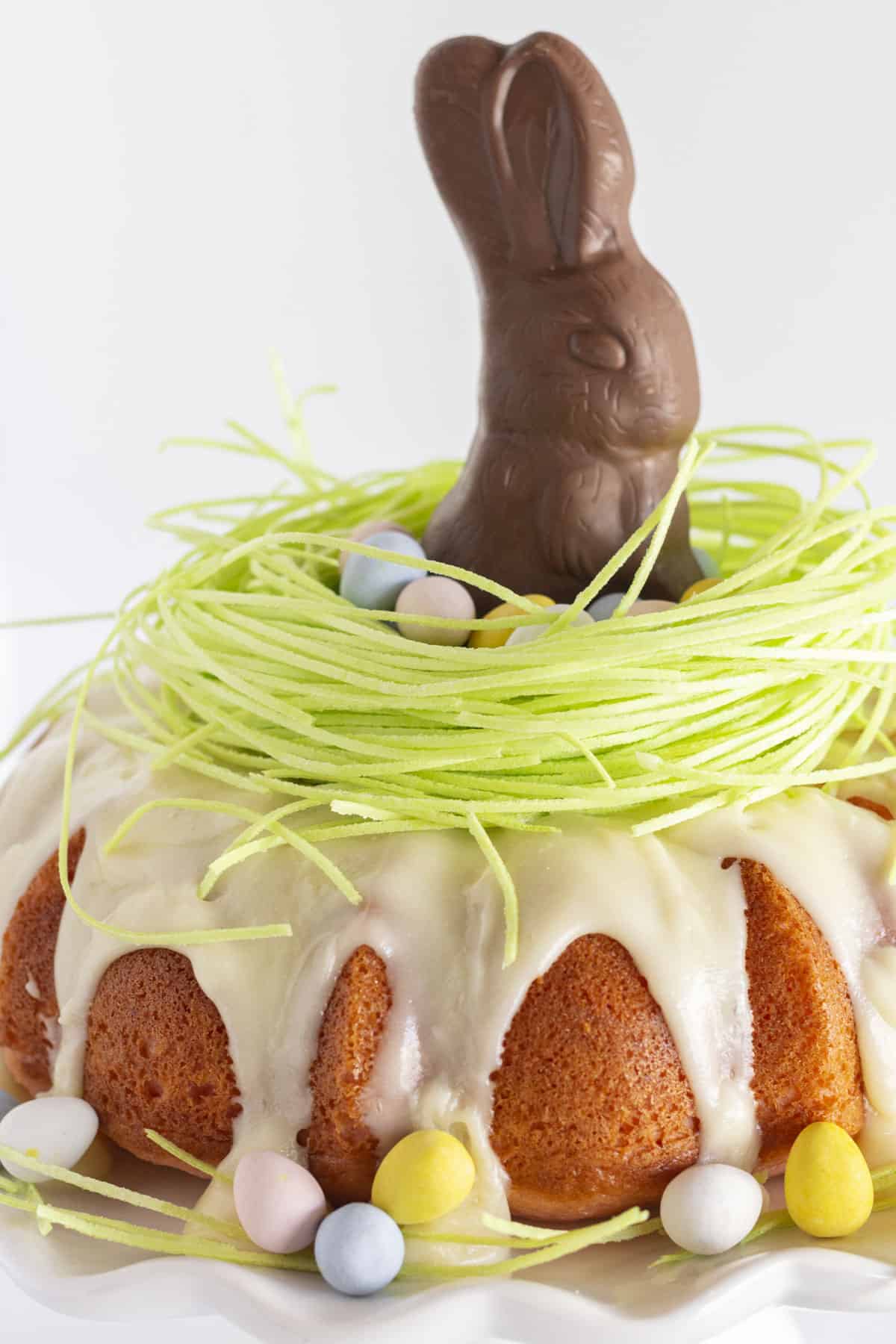 A pink velvet bundt cake decorated with edible grass and a chocolate bunny.