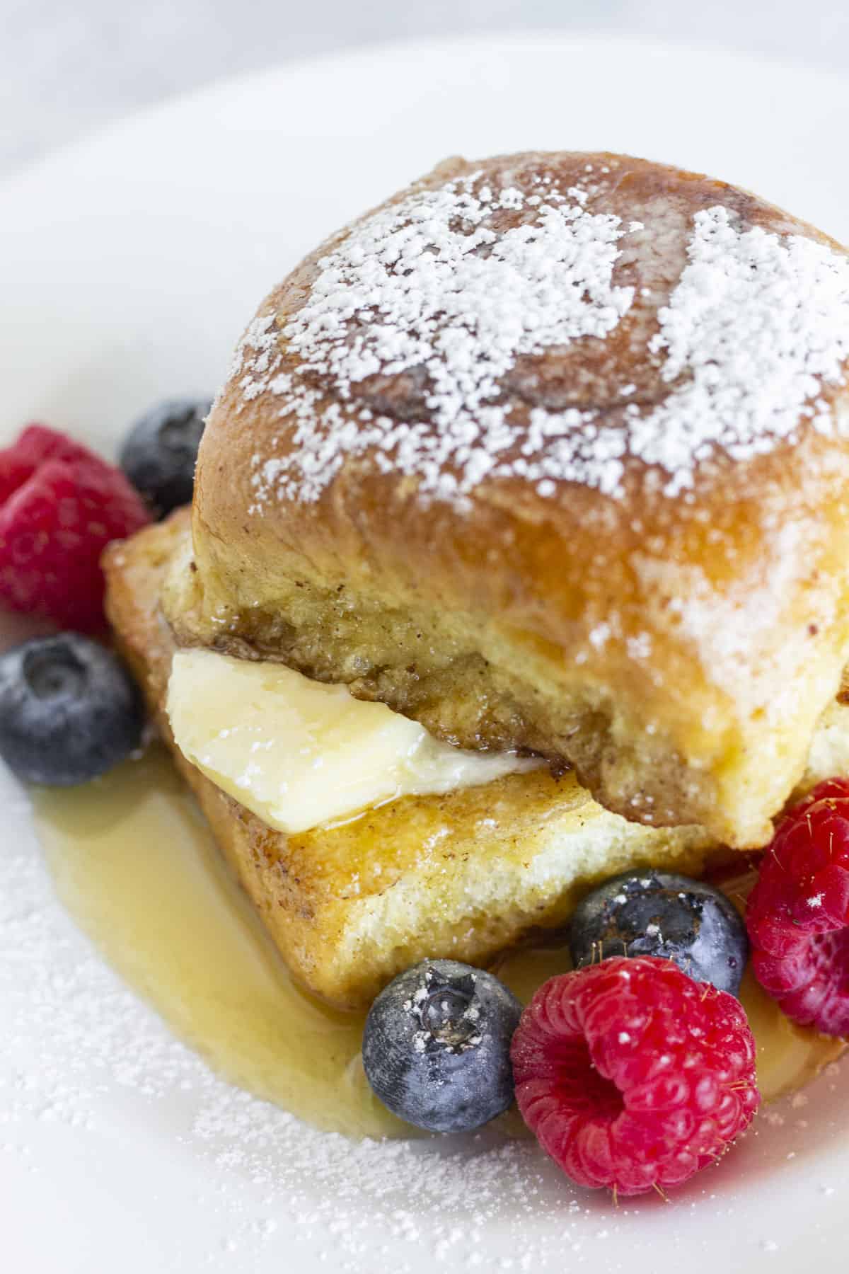 A serving of Hawaiian Roll French Toast with butter, syrup, fresh fruit and a sprinkle of powdered sugar.