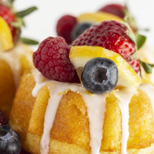 Mini lemon bundt cakes on a red cake plate with fresh fruit.