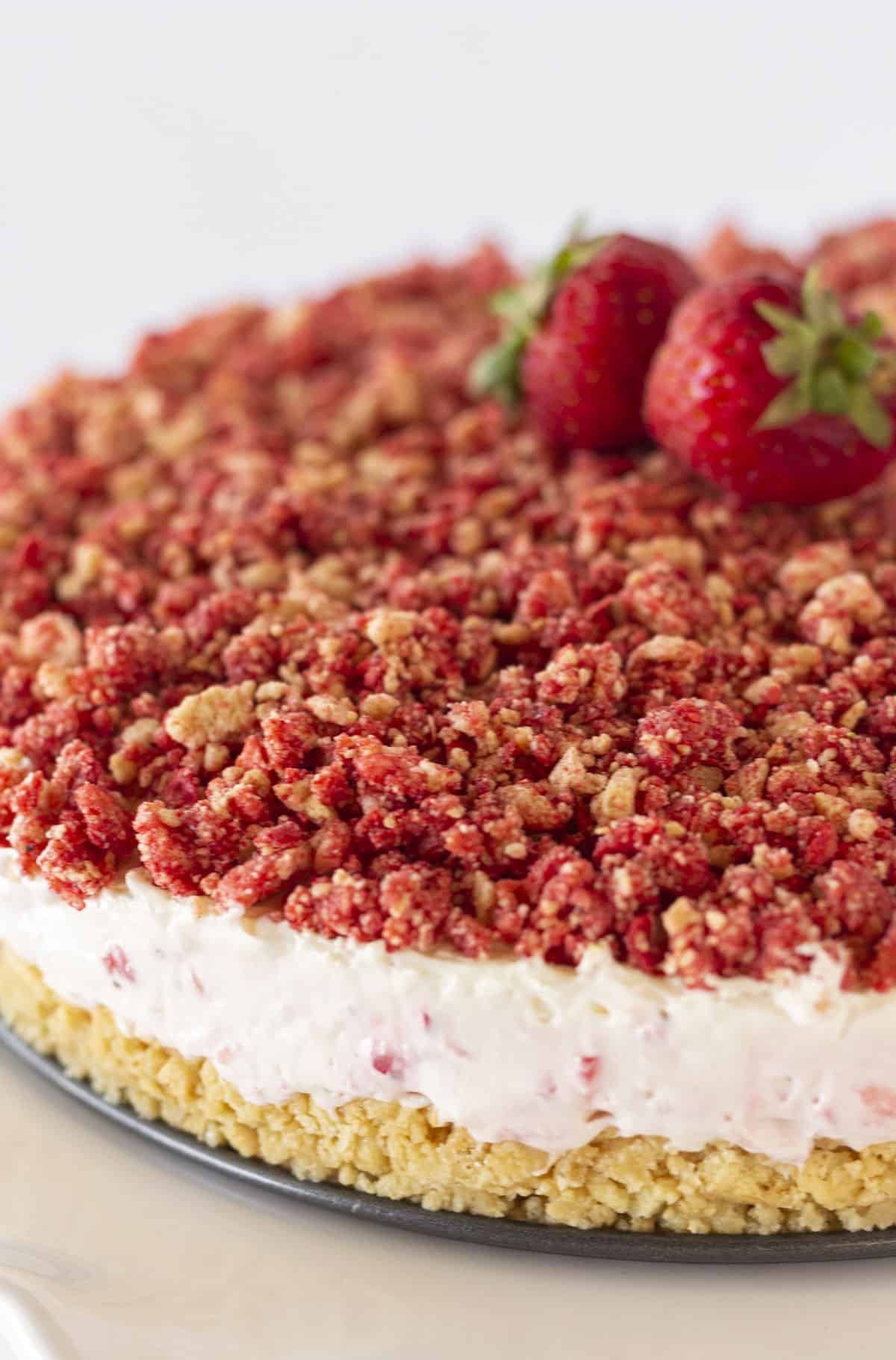 A whole strawberry crunch cheesecake with fresh strawberries on top.
