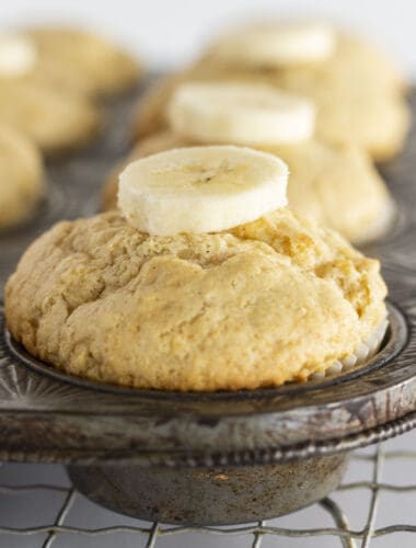 Bisquick Banana Muffins in a muffin tin with a fresh banana slice on top.