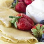 A plate of crepes with fruit and whipped cream.
