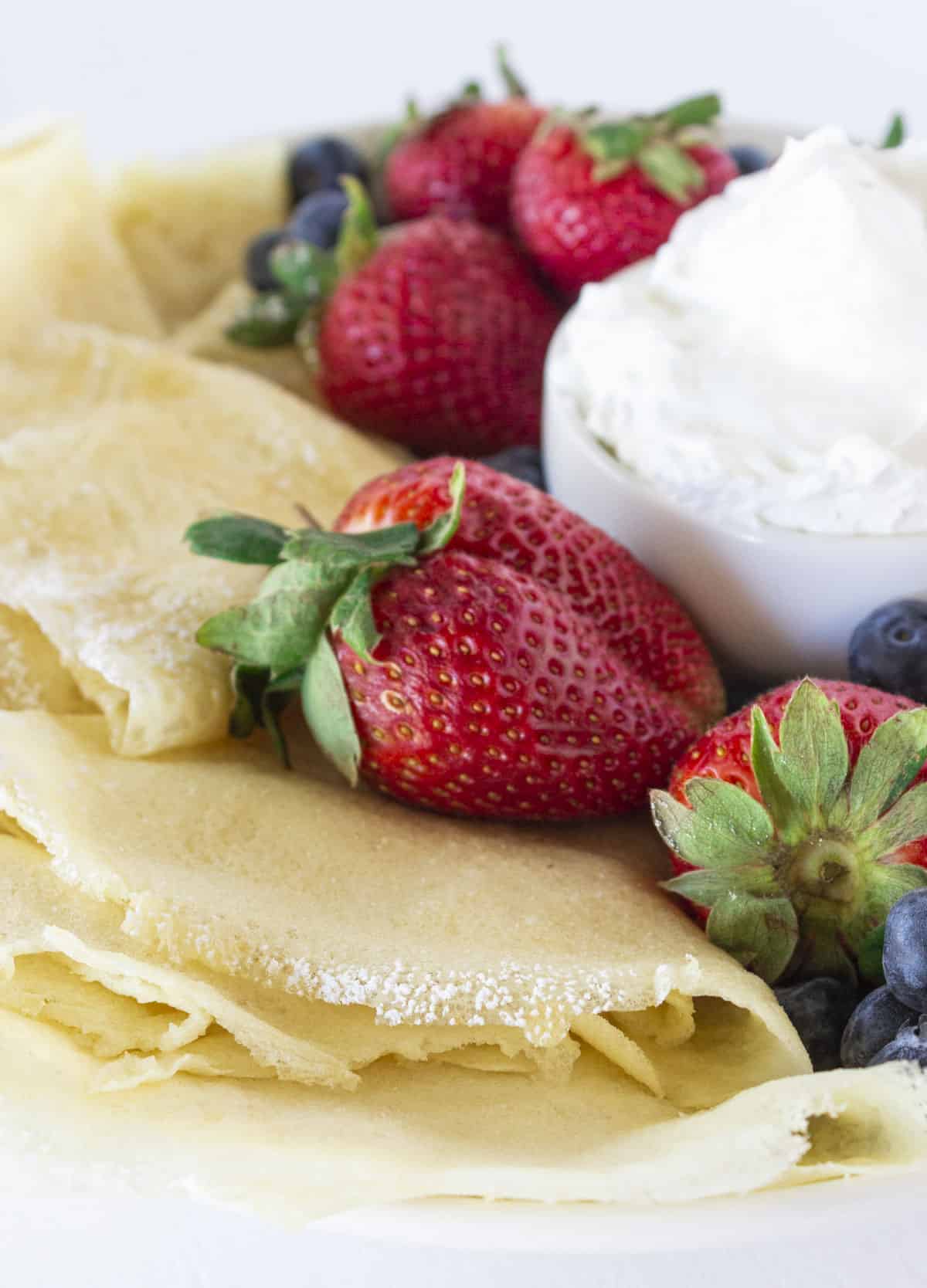 A plate full of pancake mix crepes, fresh fruit and whipped cream.