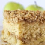 A square of apple crumb cake with a couple fresh apples in the background.