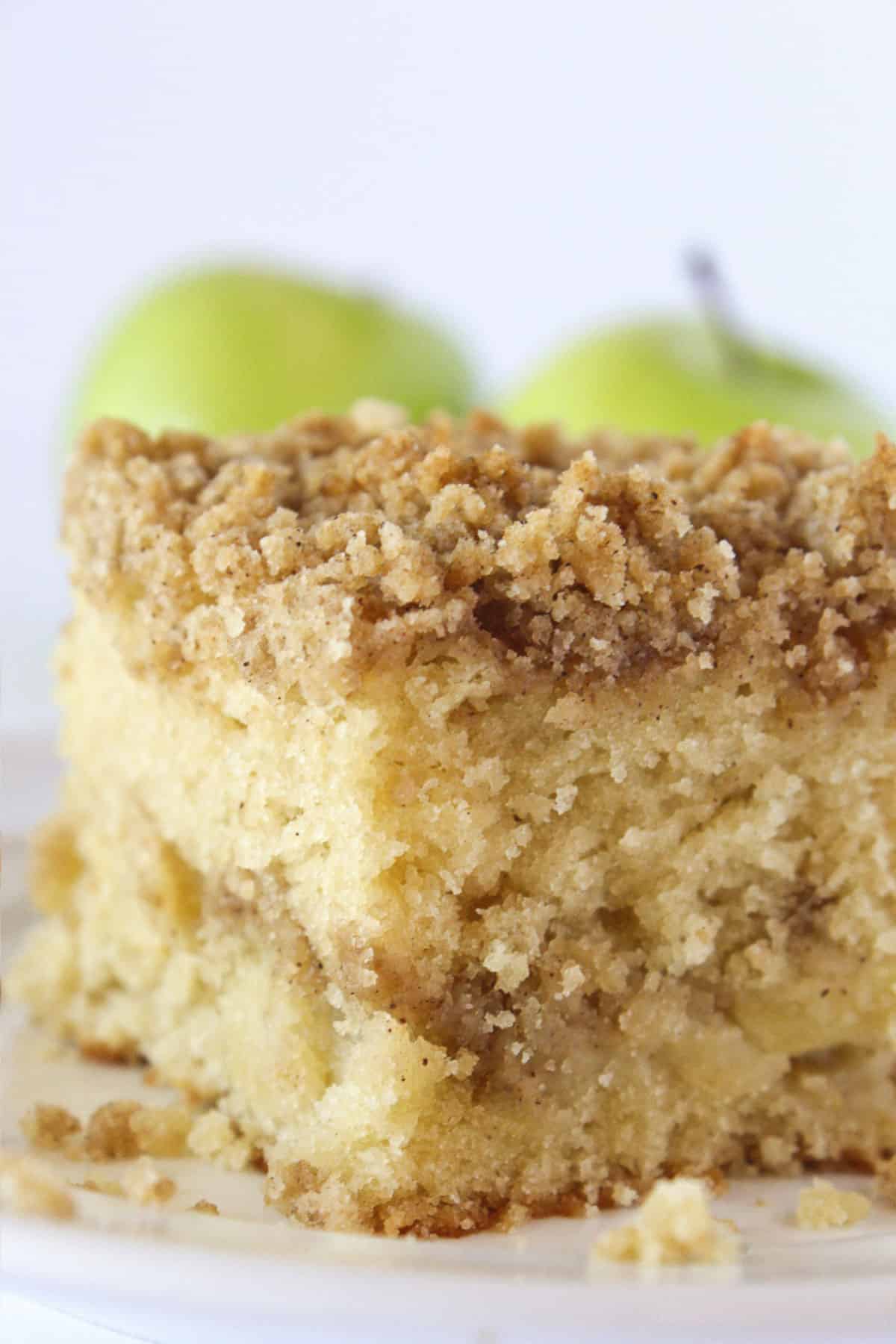 A square of apple crumb cake with a couple fresh apples in the background.