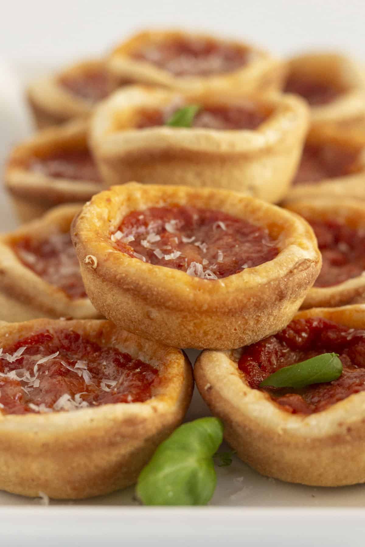 A plate full of mini deep dish pizzas with a few basil leaves.
