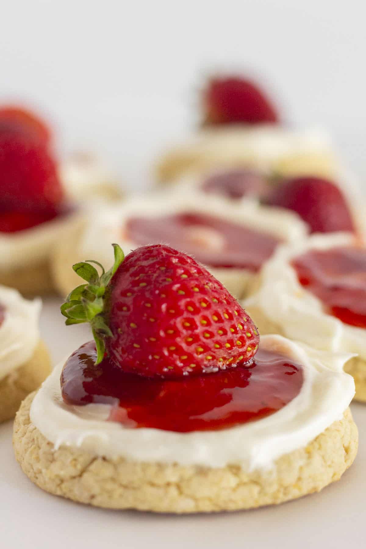 A dozen strawberry cheesecake cookies with a fresh strawberry on top.