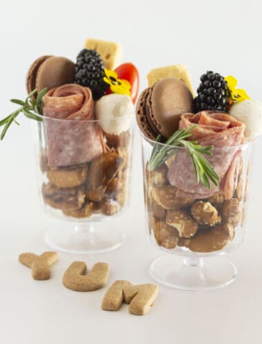 Two individual charcuterie cups filled with food and served in a clear glass.
