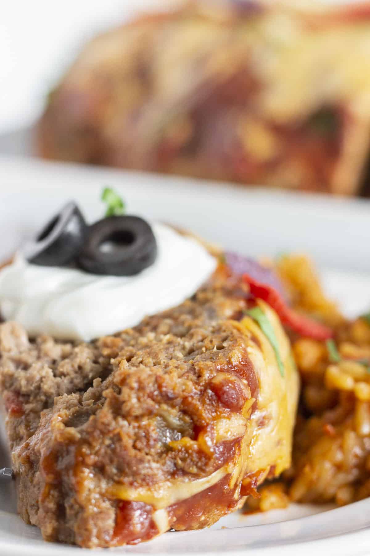 A slice of taco meatloaf with sour cream and olives on top.