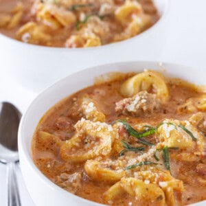 Two bowls of Tortellini Sausage Soup with parmesan and basil.
