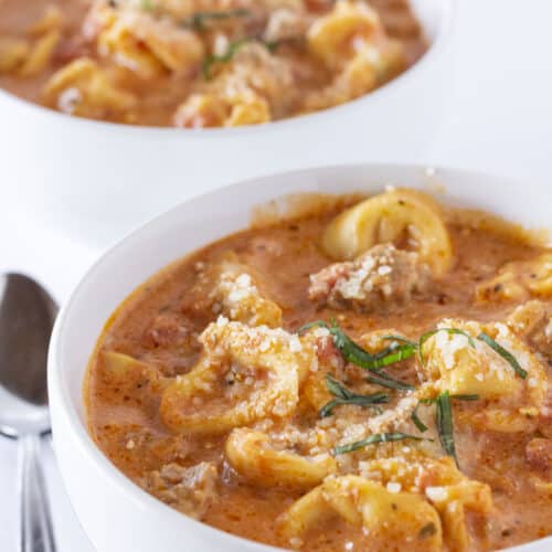 Two bowls of Tortellini Sausage Soup with parmesan and basil.