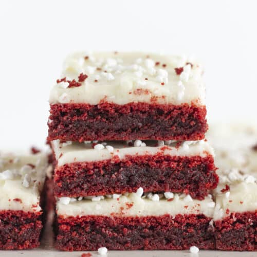 Three red velvet brownies with cream cheese frosting stacked on each other.