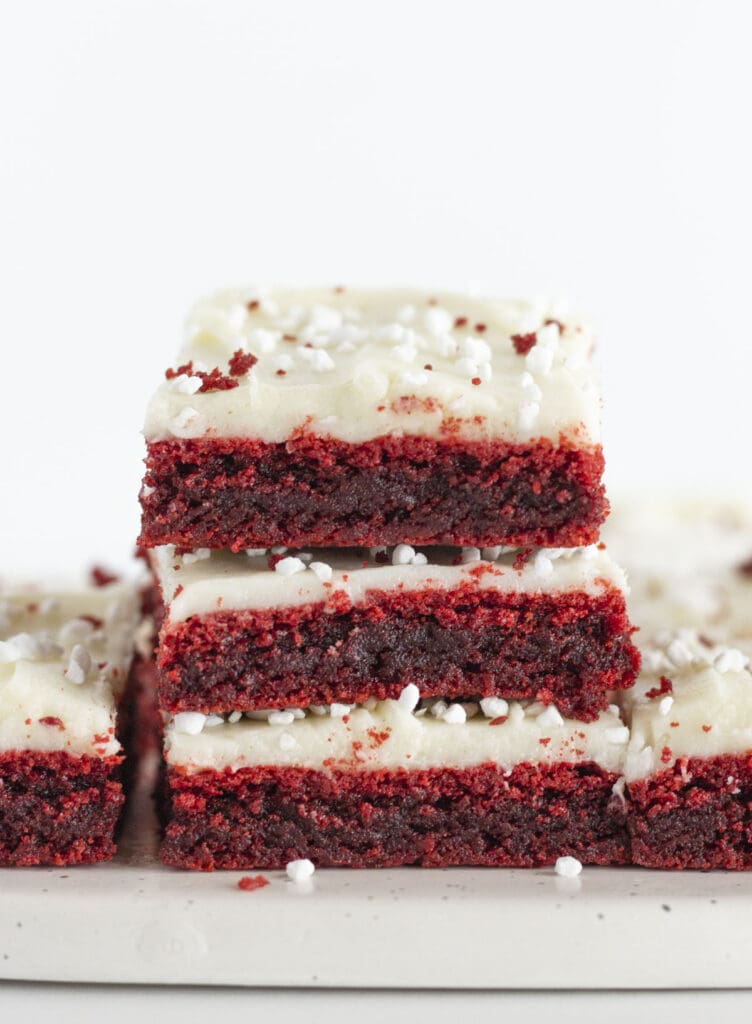 Three red velvet brownies with cream cheese frosting stacked on each other.