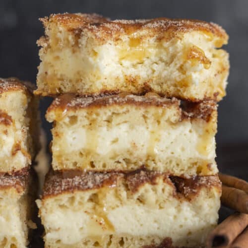 A stack of Churro Cheesecake Bars with a drizzle of caramel sauce.