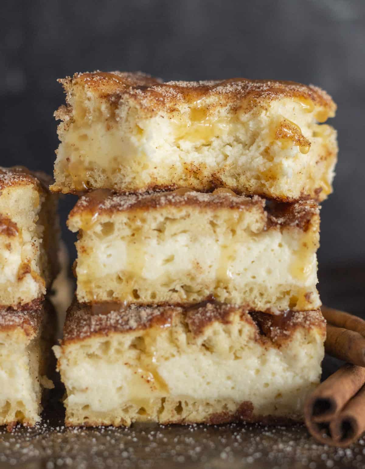 Churro cheesecake bars stacked on each other with caramel sauce.