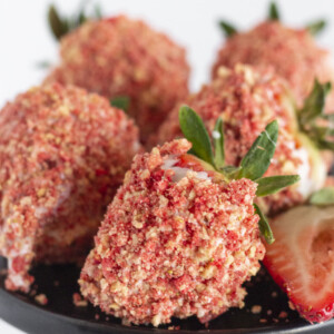 Chocolate covered strawberries with strawberry crunch topping on a black cake plate.