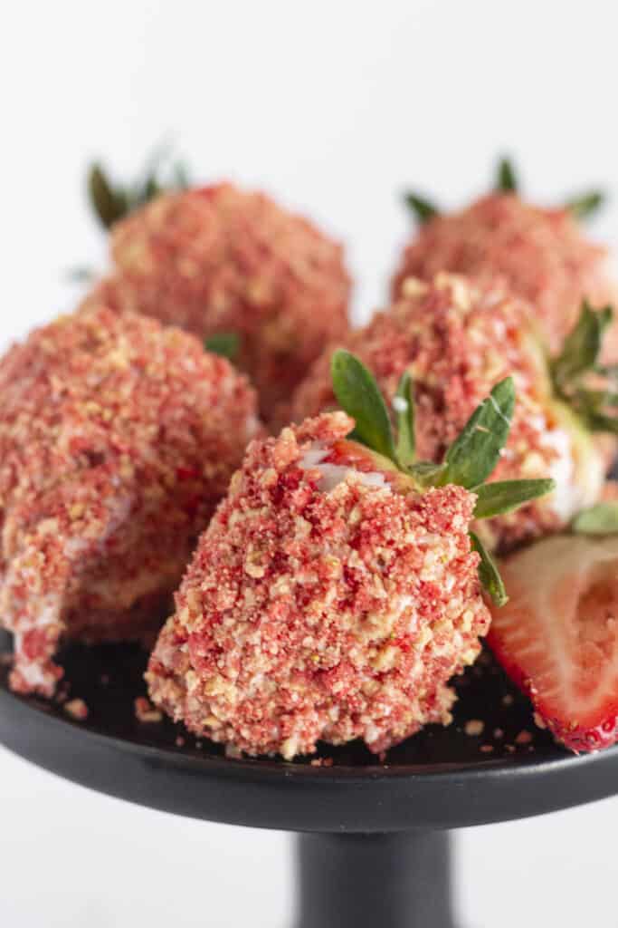 Chocolate covered strawberries with strawberry crunch topping on a black cake plate.