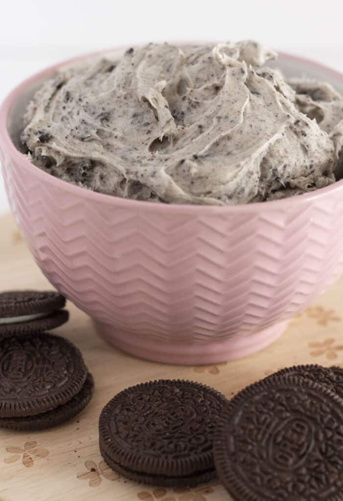 Cookies and cream frosting in a pink bowl with Oreo cookies around it.