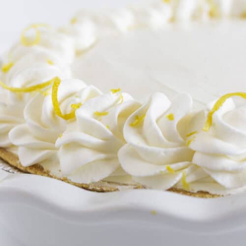 A finished no bake lemon cheesecake with whipped cream and lemon zest.