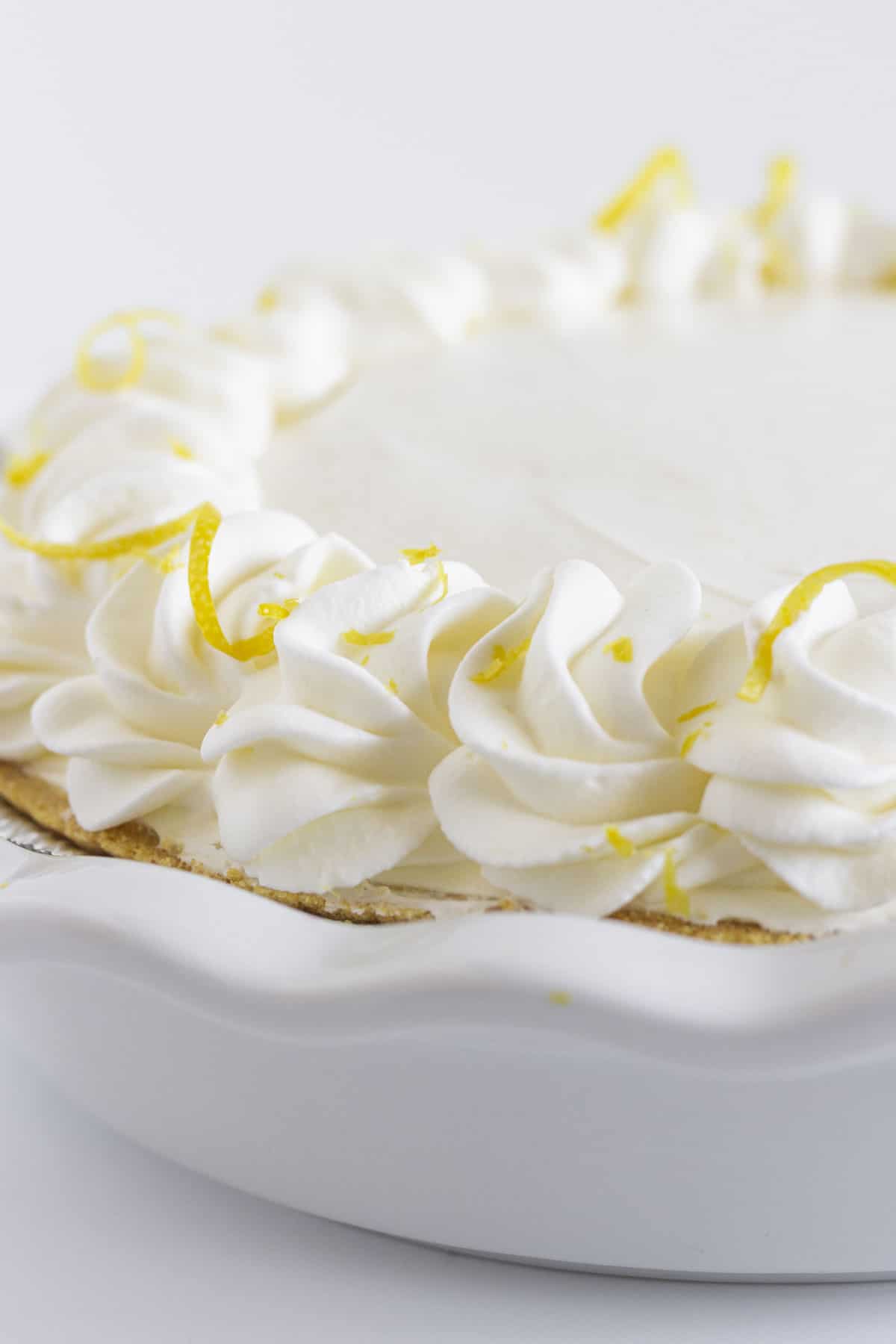 A no bake lemon cheesecake with a whipped cream border and lemon zest.
